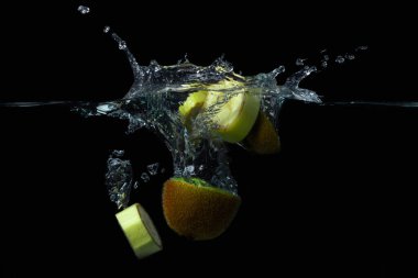 Kivi ve muz dilimleri siyah arka planda suya düşer. Dilimlenmiş meyve