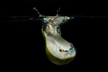 Armutun yarısı siyah arka planda suya düşer. Armut ikiye bölünmüş. Sağlıklı beslenme