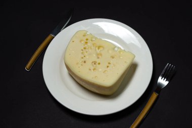 Siyah arka planda sarı peynir. Koyu arkaplanda beyaz tabakta delikleri olan bir peynir dilimi.