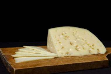 Siyah arka planda sarı peynir. Koyu arkaplanda tahta üzerinde delikleri olan bir peynir dilimi.