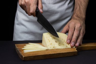 Siyah arka planda sarı peynir. Şef peyniri koyu bir arka planda keser..