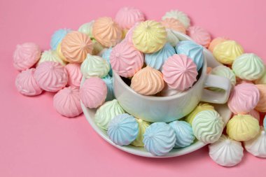 Pembe arka planda çok renkli kremalar. Renkli kremalarla dolu bir çay fincanı..