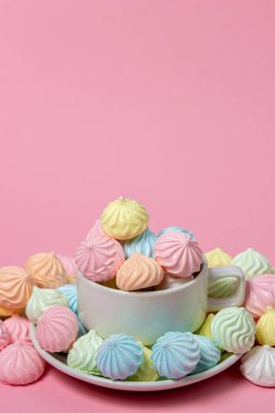 Pembe arka planda çok renkli kremalar. Renkli kremalarla dolu bir çay fincanı..