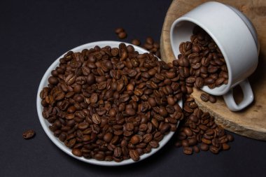 Siyah arka planda kahve çekirdekleri ile dolu bir fincan. Bardaktan taze kavrulmuş kahve çekirdekleri dökülüyor. Aşırı kafein tüketimi