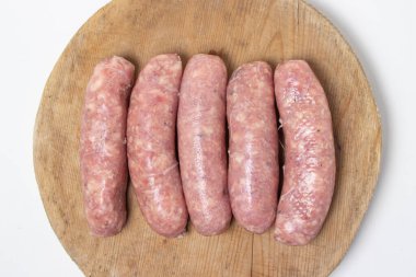 Beyaz arka planda tahta bir tahtada çiğ et sosisi. Doğal kaplamalı ev yapımı sosisler. Et ürünleri