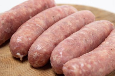 Beyaz arka planda tahta bir tahtada çiğ et sosisi. Doğal kaplamalı ev yapımı sosisler. Et ürünleri