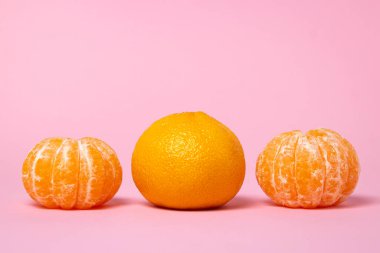 Pembe arka planda soyulmamış mandalinaların yanında soyulmuş mandalina. Renkli arkaplanda turunç meyvesi