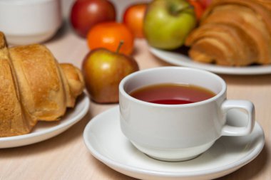 Beyaz bir masada lezzetli ve sağlıklı bir kahvaltı. Bir fincan çay, hamur işi ve meyveli..