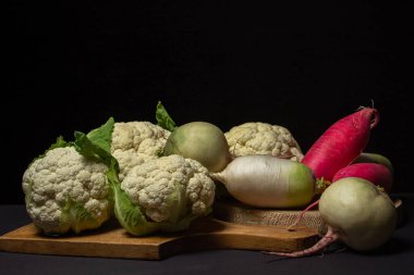 Siyah arka planda çeşitli sebzeler. Koyu arkaplanda karnabahar olan farklı turp çeşitleri. Lezzetli ve sağlıklı sebzeler. Vejetaryen yemeği. Sebze dolu bir hayat