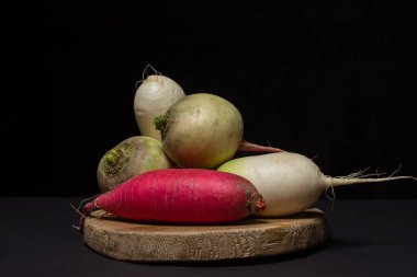 Siyah arka planda farklı turp çeşitleri. Beyaz turpun yanında uzun kırmızı turp. Lezzetli ve sağlıklı sebzeler. Vejetaryen yemeği..