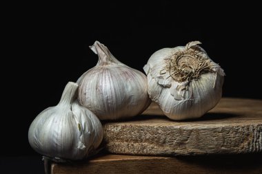 Siyah arka planda sarımsak. Koyu arkaplanda tahta üzerinde üç baş sarımsak. Sağlıklı sebzeler