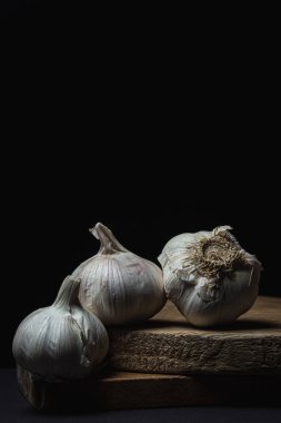 Siyah arka planda sarımsak. Koyu arkaplanda tahta üzerinde üç baş sarımsak. Sağlıklı sebzeler
