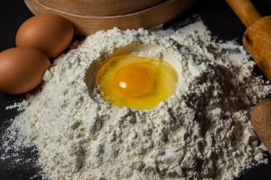 Siyah arka planda un içinde çiğ yumurta. Hamur hazırlığı. Ev yapımı pişirme