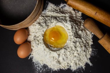 Siyah arka planda un içinde çiğ yumurta. Hamur hazırlığı. Ev yapımı pişirme