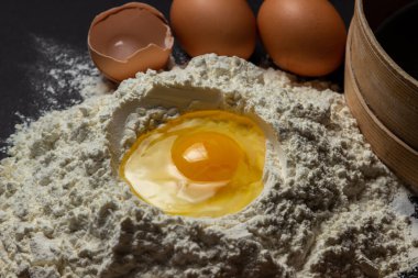 Siyah arka planda un içinde çiğ yumurta. Hamur hazırlığı. Ev yapımı pişirme