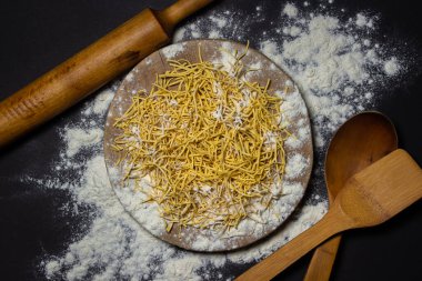 Egg noodles in flour on a black background. Dry homemade noodles on a wooden board. Traditional pasta