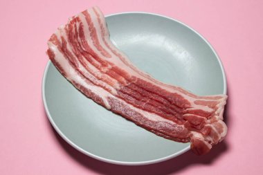 Pembe arka planda pastırma. Tabakta çiğ domuz pastırması. Taze domuz eti.