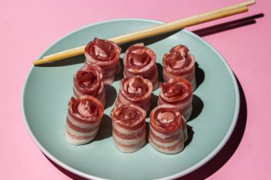 Pembe arka planda pastırma. Tabakta çiğ domuz pastırması. Çin çubukları et parçalarının yanında. Domuz eti. Pastırma