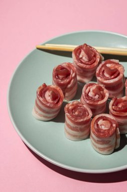 Pembe arka planda pastırma. Tabakta çiğ domuz pastırması. Çin çubukları et parçalarının yanında. Domuz eti. Pastırma