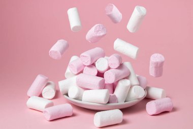 Pembe arka planda şekerlemeler. Marşmelovlar şekerleme dolu bir tabağa düşer. Tatlı çok lezzetli.