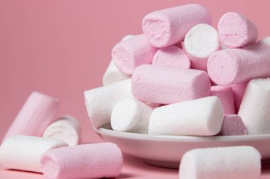 Pembe arka planda şekerlemeler. Beyaz bir tabakta renkli şekerlemeler. Tatlı çok lezzetli.