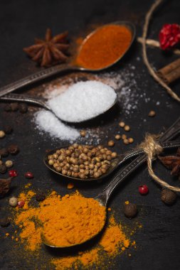 Siyah arka planda baharatlar. Karanlık bir yüzeyde farklı baharatlı kaşıklar. geleneksel baharatlar