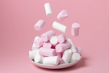 Pembe arka planda şekerlemeler. Marşmelovlar şekerleme dolu bir tabağa düşer. Tatlı çok lezzetli.
