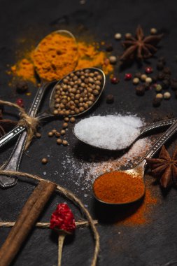 Siyah arka planda baharatlar. Karanlık bir yüzeyde farklı baharatlı kaşıklar. geleneksel baharatlar