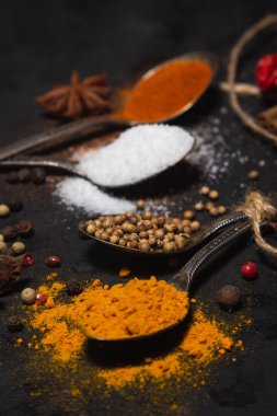 Siyah arka planda baharatlar. Karanlık bir yüzeyde farklı baharatlı kaşıklar. geleneksel baharatlar