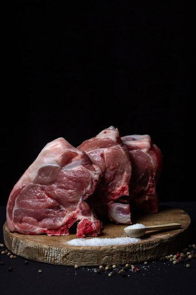 Pork meat on a black background. Meat loin with bone on a wooden board. Meat cooking