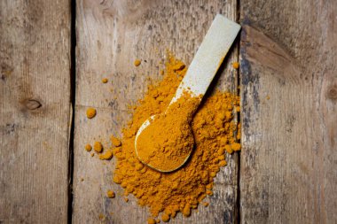 Ahşap arka planda zemin zerrecikleri. Masada bir kaşık zerdeçal var. Geleneksel baharatlar.