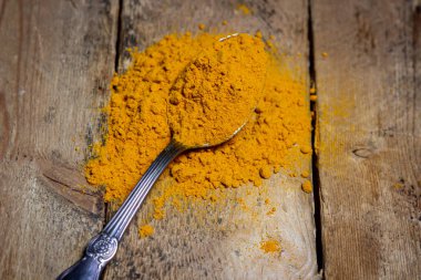 Ahşap arka planda zemin zerrecikleri. Masada bir kaşık zerdeçal var. Geleneksel baharatlar.