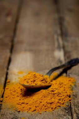 Ahşap arka planda zemin zerrecikleri. Masada bir kaşık zerdeçal var. Geleneksel baharatlar.