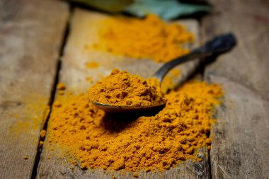 Ahşap arka planda zemin zerrecikleri. Masada bir kaşık zerdeçal var. Geleneksel baharatlar.