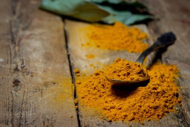 Ahşap arka planda zemin zerrecikleri. Masada bir kaşık zerdeçal var. Geleneksel baharatlar.