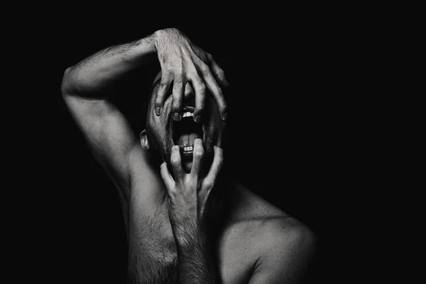 Korku tarzında erkek portresi. Siyah arka planda siyah beyaz erkek portresi. Adam elleriyle çenesini açar.