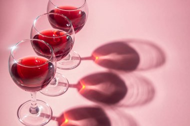Pembe arka planda kırmızı şarap kadehleri. Alkolik içki..