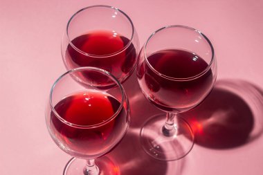 Pembe arka planda kırmızı şarap kadehleri. Alkolik içki..