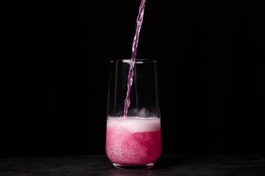 Pembe içecek siyah arka planda bir bardağa dökülür. Karbonatlı tatlı su. Lezzetli içecek