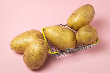 Pembe arka planda alışveriş sepetindeki genç patatesler. Çiğ sarı patates. Yeni mahsul