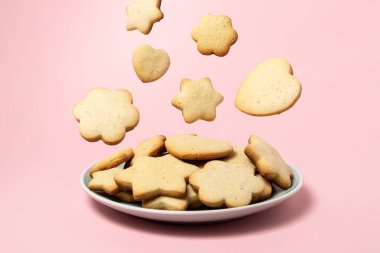 Cookies fall into a plate with cookies on a pink background. Homemade shortbread cookies. Delicious and light dessert. clipart