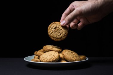 Bir el siyah arka planda yulaflı kurabiye yer. Hafif ve lezzetli bir tatlı. Sağlıklı kahvaltı.