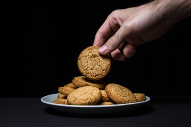 Bir el siyah arka planda yulaflı kurabiye yer. Hafif ve lezzetli bir tatlı. Sağlıklı kahvaltı.