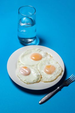 Mavi arka planda sahanda yumurta. Bir tabakta üç yumurta. Hızlı ve lezzetli bir kahvaltı.