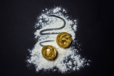 Makarna siyah arka planda un üzerine yuva yapar. Makarna şekli. Geleneksel yemek
