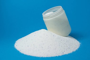 Mavi arka planda çamaşır deterjanı. Ölçüm kabı deterjanla dolu. Ev kimyasalları.