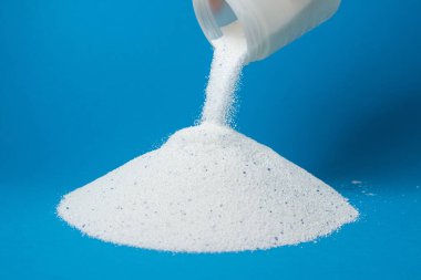 Mavi arka planda çamaşır deterjanı. Yıkama tozu bir çamaşır tozu yığını üzerine serpilmiş. Ev kimyasalları.