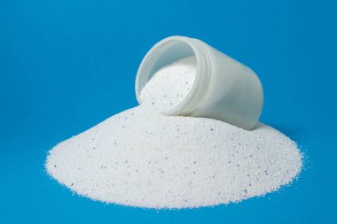 Mavi arka planda çamaşır deterjanı. Ölçüm kabı deterjanla dolu. Ev kimyasalları.