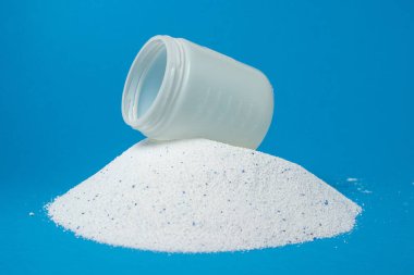 Mavi arka planda çamaşır deterjanı. Çamaşır deterjanı yığını üzerindeki ölçü kabı. Ev kimyasalları.