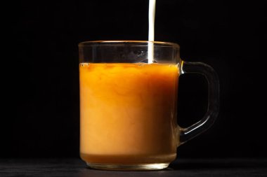 Siyah arka planda sütlü çay. Süt, çay ile şeffaf bir bardağa dökülür. Geleneksel içki.